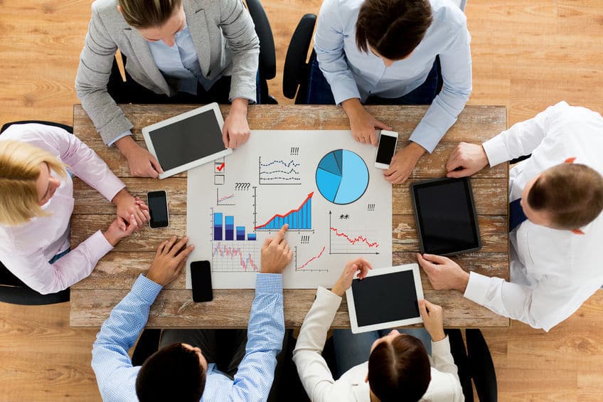 business, people, statistics and team work concept - close up of creative team with charts on paper, smartphones and tablet pc computers sitting at table in office